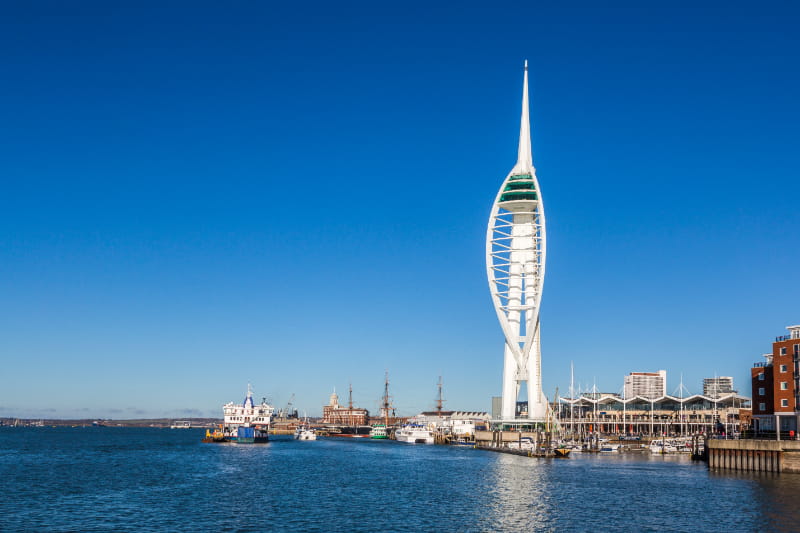 a large clock tower in the middle of a body of water with Spinnaker Tower in the background