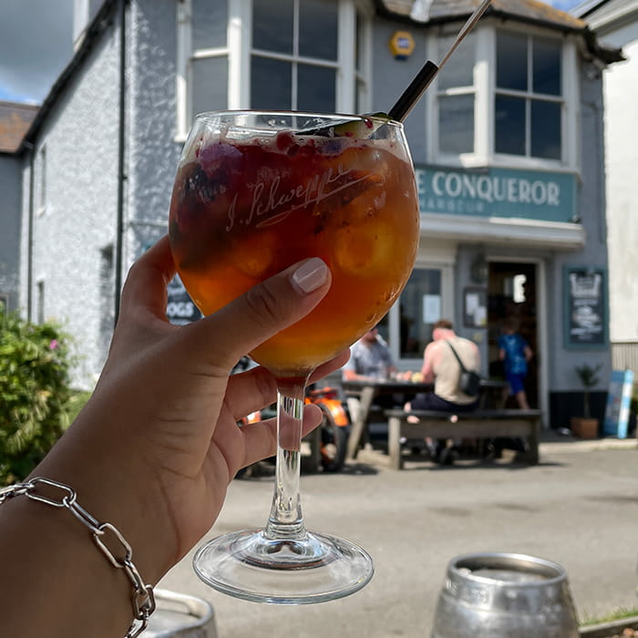 Closeup of a hand holding a glass of Pimms with a pub in the background