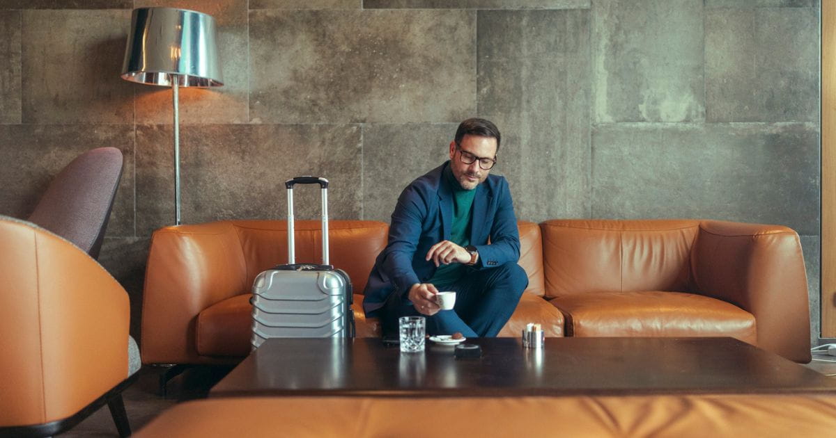 Smart man with luggage enjoying a drink in an airport lounge